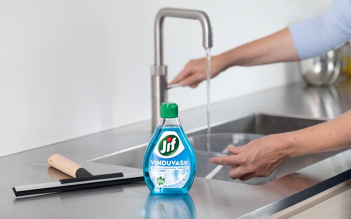 Kvinne fyller vaskebøtte med vann og Jif Vindu Vask.